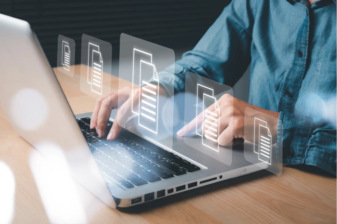 Man typing on a computer with see through document holograms to show that he is working on invoices and documents. 